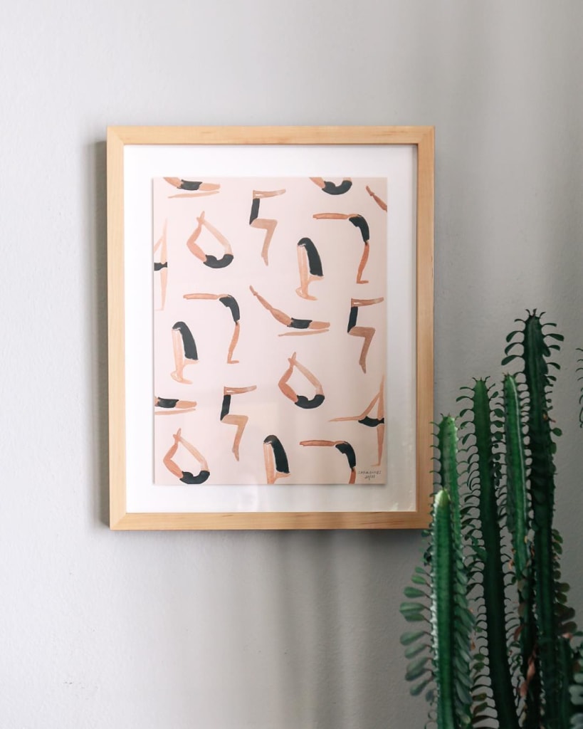 abstract yoga art painting of people doing yoga with beige frame and hanging beside a tall cactus